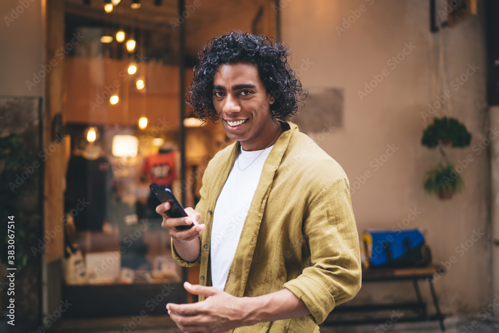 Happy young ethnic man browsing cellphone near entrance of shop Happy young ethnic man browsing cellphone near entrance of shop