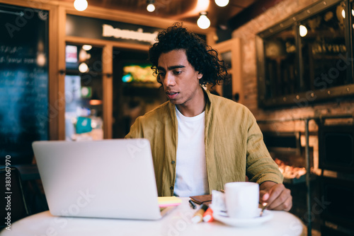 Focused ethnic man using laptop in cafe