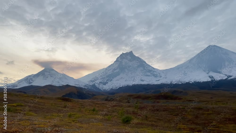 An epic aerial view of three volcanoes in central Kamchatka: Bezymyanny volcano (smokes), Kamen volcano and Klyuchevskaya volcano. Space landscapes of Kamchatka. Autumn tundra. An epic aerial view of three volcanoes in central Kamchatka: Bezymyanny volcano (smokes), Kamen volcano and Klyuchevskaya volcano. Space landscapes of Kamchatka. Autumn tundra.