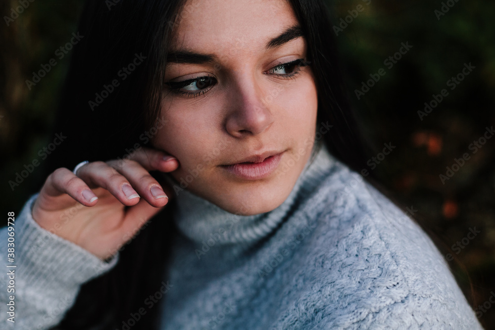 portrait of a white woman touching her cheek, she is wearing gray sweater in the middle of nature portrait of a white woman touching her cheek, she is wearing gray sweater in the middle of nature