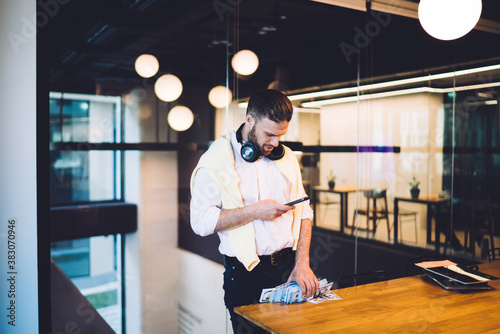 Smart casual coworker using cellphone device for checking income dividend during stock exchange during money making, Caucasian businessman with dollars wad writing email message about earnings photo