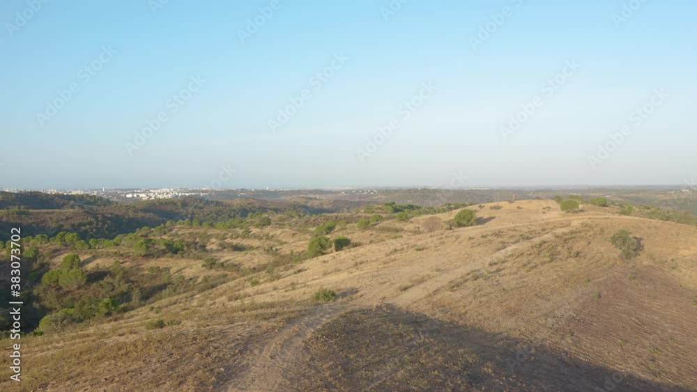 Aerial tracking shot backwards of dirt trail on top of a barren hill in Algarve, Portugal