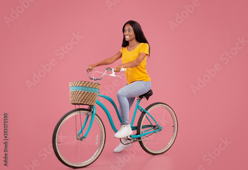 Full length portrait of pretty black woman in casual clothes riding vintage bicycle on pink studio background © Prostock-studio