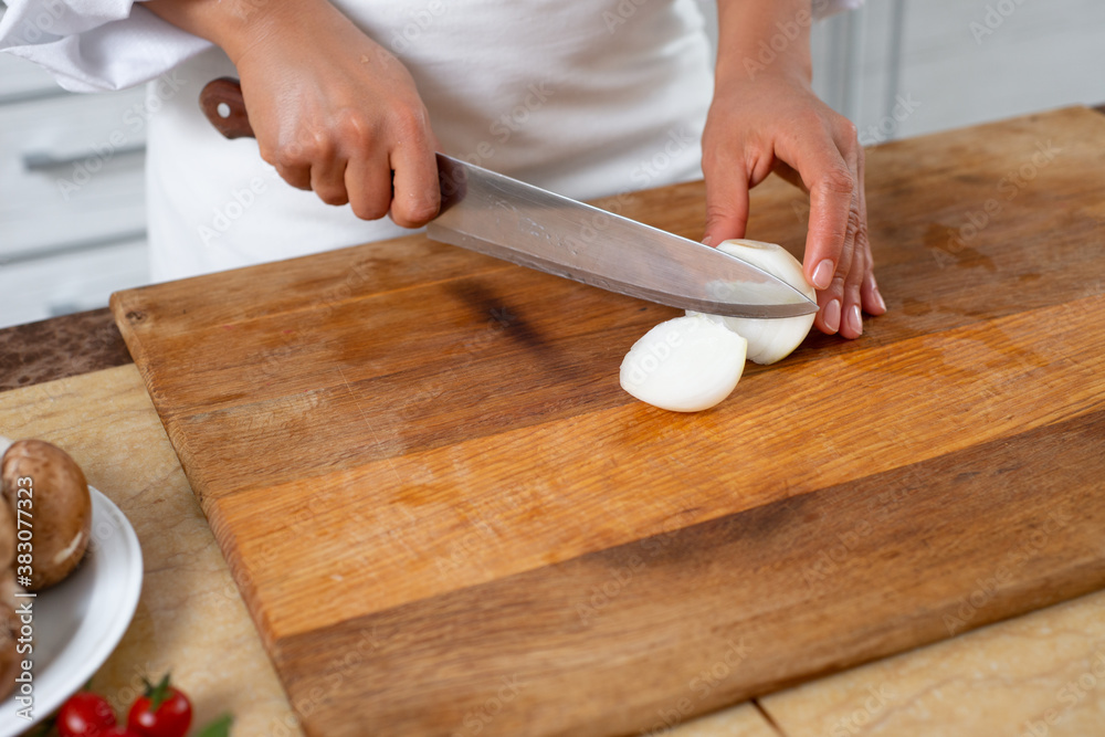 Close-up, the chef cuts the onion with a knife on a wooden board.