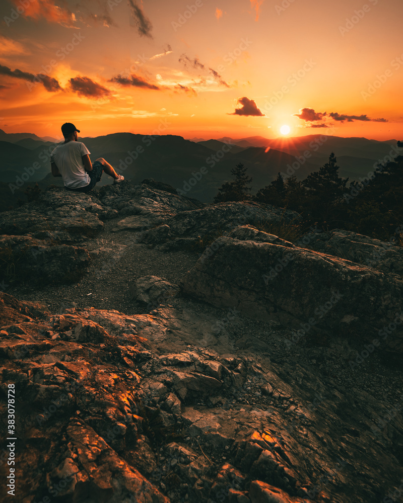 Obraz premium Hiker with backpack sitting on mountain and enjoying sunset