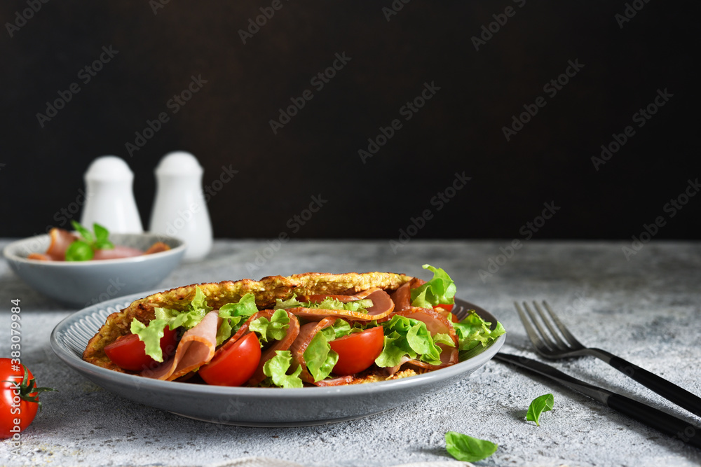 Pancake with ham, salad and tomatoes on a concrete gray background. Breakfast on the kitchen table.