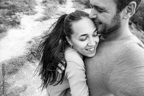 Black and white selfie photo of a happy couple in love. A man and a woman hug with their eyes closed and laugh.