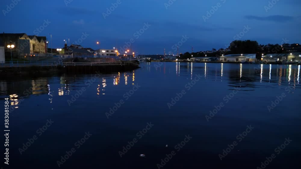 Town lights reflections on dark blue rippled water of Welsh Milford Haven marina at night; some litter floating. Town lights reflections on dark blue rippled water of Welsh Milford Haven marina at night; some litter floating.