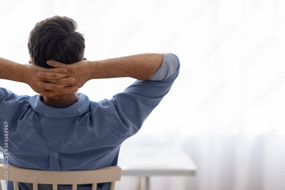 Rear view of man leaning back on chair with hands behind head Rear view of man leaning back on chair with hands behind head