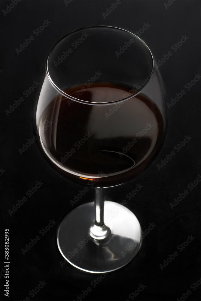 A glass of red wine on a dark background. A glass of red wine on a dark background.