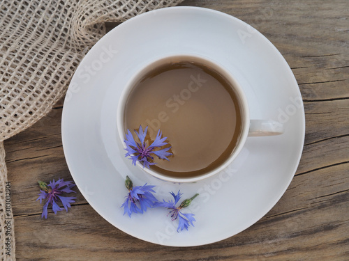 Herbal tea in a white   up with a saucer and flowers of a useful plant blue cornflower with a napkin on a wooden stand  top view. Medical herb centaurea cyanus with blue flowers for use in medicine
