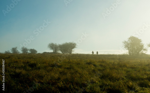 Silhouettes of 2 people walking during early morning on Butser Hill, Hampshire.
