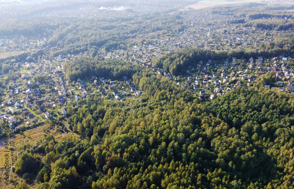 Fototapeta premium Beautiful top view of suburban cottages with park and forest. Rural landscape with roofs of small houses and villages