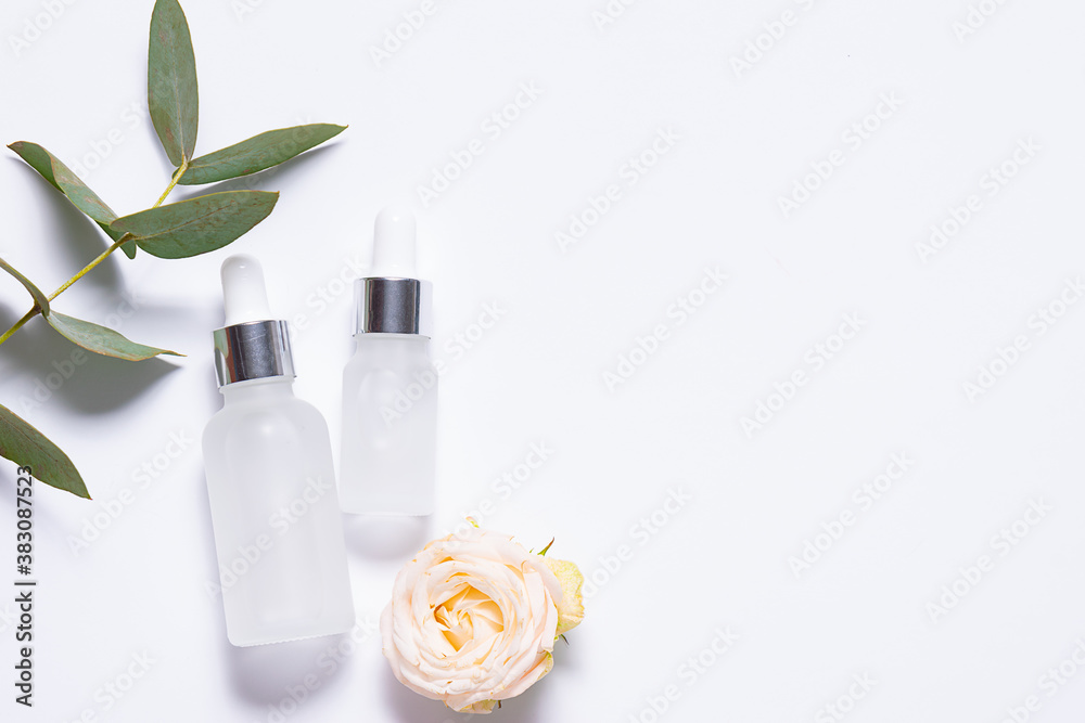 Organic serums for skin care in glass white bottles on white background with eucalyptus twig and rose flower. Face care concept. Organic serums for skin care in glass white bottles on white background with eucalyptus twig and rose flower. Face care concept.