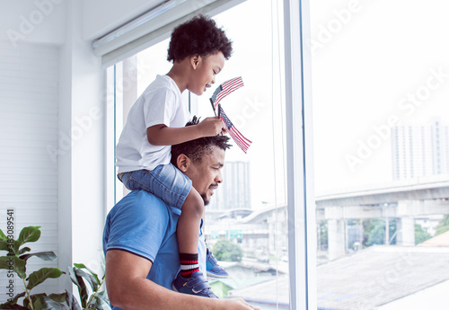 A father carrying his african black son while a boy waving american flag photo