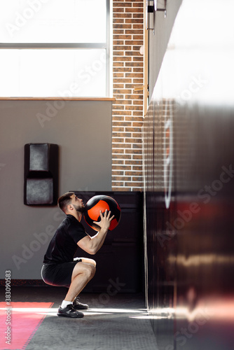 Wall ball training. Young athlete doing wall ball exercise at gym. Crossfit workout concept