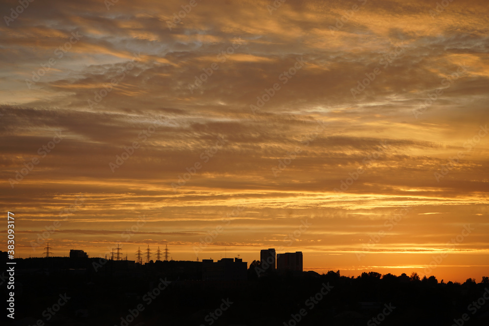 Golden sunset over the city. Silhouettes of buildings and trees on the horizon against the background of the sky with clouds. Colorful orange yellow red sunset background.