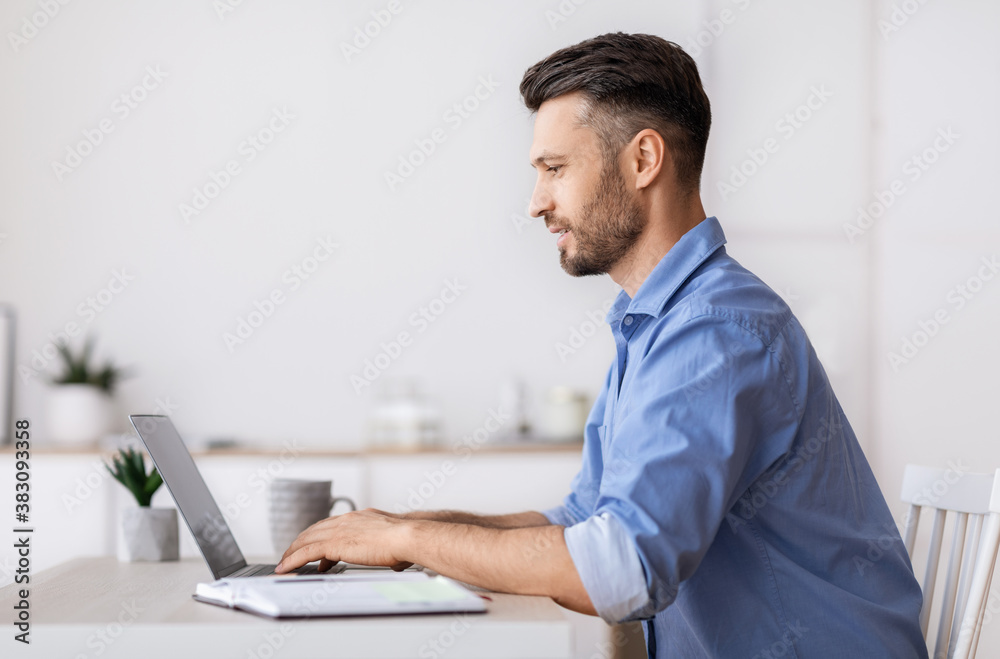 Handsome millennial businessman sitting at workplace in office, working on laptop Handsome millennial businessman sitting at workplace in office, working on laptop