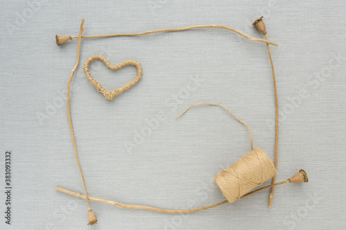 Heart of jute handmade, spool of jute twine in frame from dried flowers, on grey background. flat lay. mock up. copy space. Greeting card. ecology, handmade, romance, holidays, valentines day concept