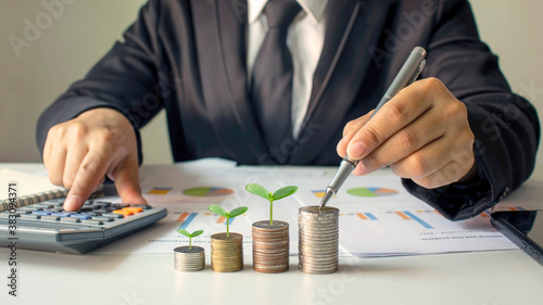 Businessman pointing to a stack of coins where plants are growing, business and financial growth ideas.