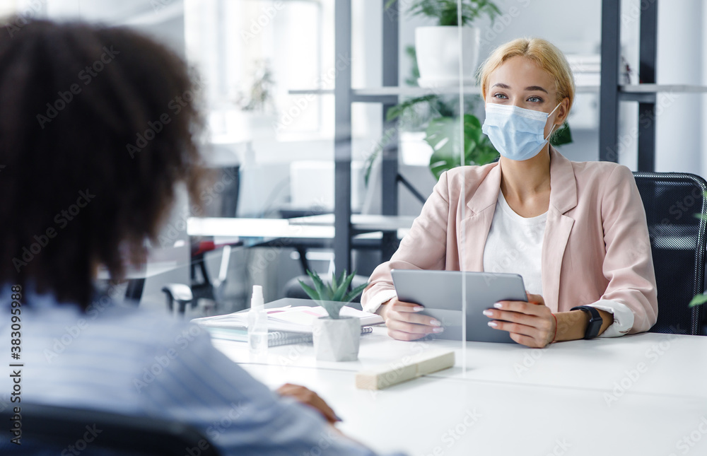 New normal and modern interview during covid-19 outbreak. HR manager with laptop looks at african american woman through protective glass New normal and modern interview during covid-19 outbreak. HR manager with laptop looks at african american woman through protective glass