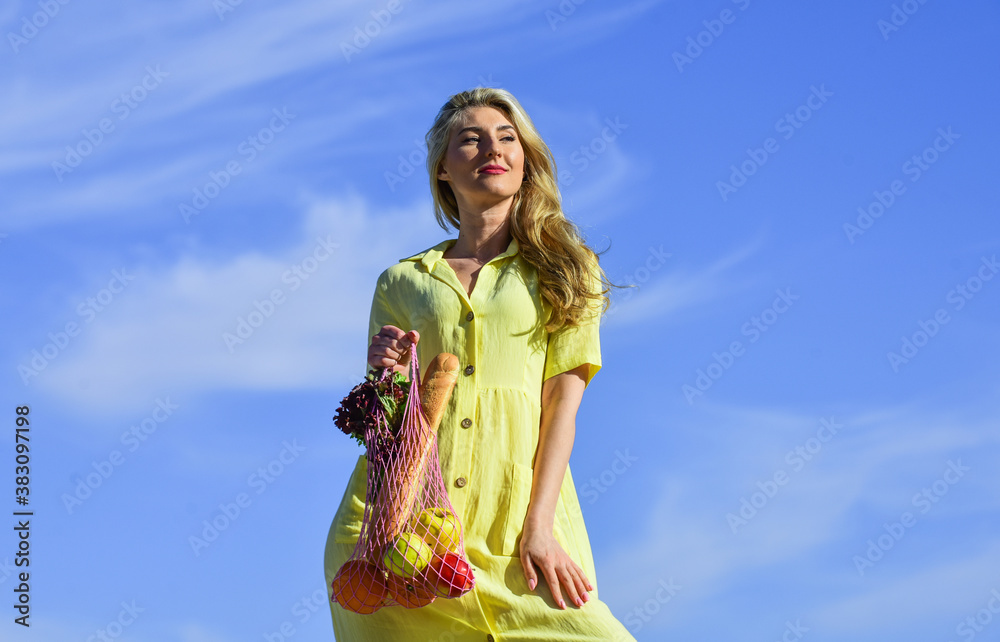 Zero waste concept. girl in dress with string bag shopper. bag with groceries. Reusable eco bag for shopping. Woman holding string shopping bag with fruits and bread on sky background. Organic food