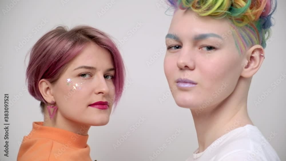 Two young girls with bright colored dyed hair and short haircuts. Hairdresser colorist and model pose against a white background, laugh and rejoice. Homosexual lesbian couple. Two young girls with bright colored dyed hair and short haircuts. Hairdresser colorist and model pose against a white background, laugh and rejoice. Homosexual lesbian couple.