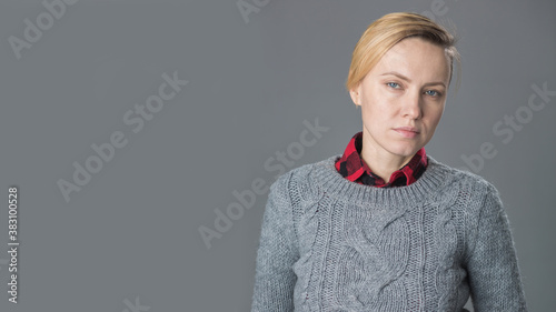 young woman with short hair, natural makeup over light grey background. Indoor portrait of beautiful blonde young woman in knitted sweater