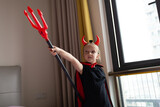 Little Girl in costume of devil with red horns at home. Happy Halloween concept