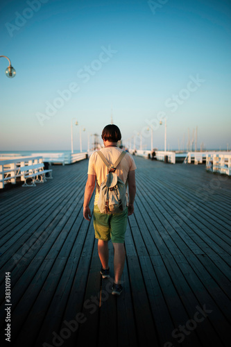 Young male tourist with vintage backpack walking on the wooden pier in golden hour