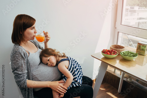 child girl sitting on the legs of a pregnant mother and communicating with the child in the woman's tummy