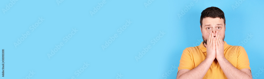 Brunette man scared, holds his hands ove mouth. Isolated on blue background, copy space template, banner. Brunette man scared, holds his hands ove mouth. Isolated on blue background, copy space template, banner.