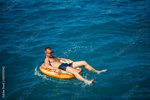 A young man swims in the open sea on an inflatable ring on a sunny day. Summer vacation, tourist on vacation © Дмитрий Ткачук