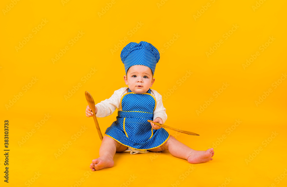 little girl in a chef costume on a yellow background with a wooden spatula and spoon little girl in a chef costume on a yellow background with a wooden spatula and spoon