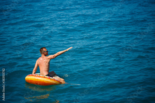 A young man floats on an inflatable air ring circle in the sea with blue water. Festive holiday on a happy sunny day. Vacation concept, top view.