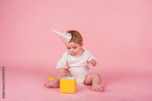 a little girl with a holiday hat is playing with a yellow box on a pink background with space for text