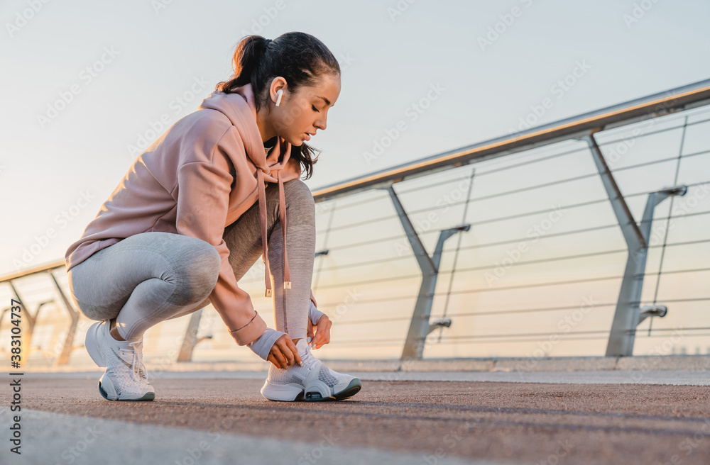 Cropped photo of female athlete tying her sneakers on the bridge