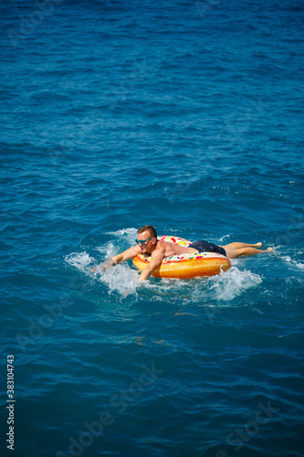 a man lies on a large inflatable rubber circle and floats on the blue sea on a bright sunny summer day