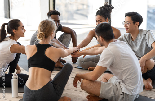 Sporty multiethnic men and women putting hands together after group yoga lesson