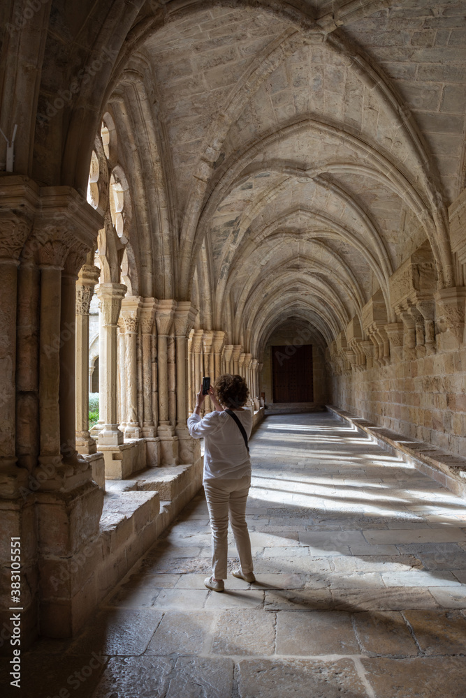 View of the cloister of the Poblet monastery with a woman on her back taking a photo with her smartphone, in vertical View of the cloister of the Poblet monastery with a woman on her back taking a photo with her smartphone, in vertical