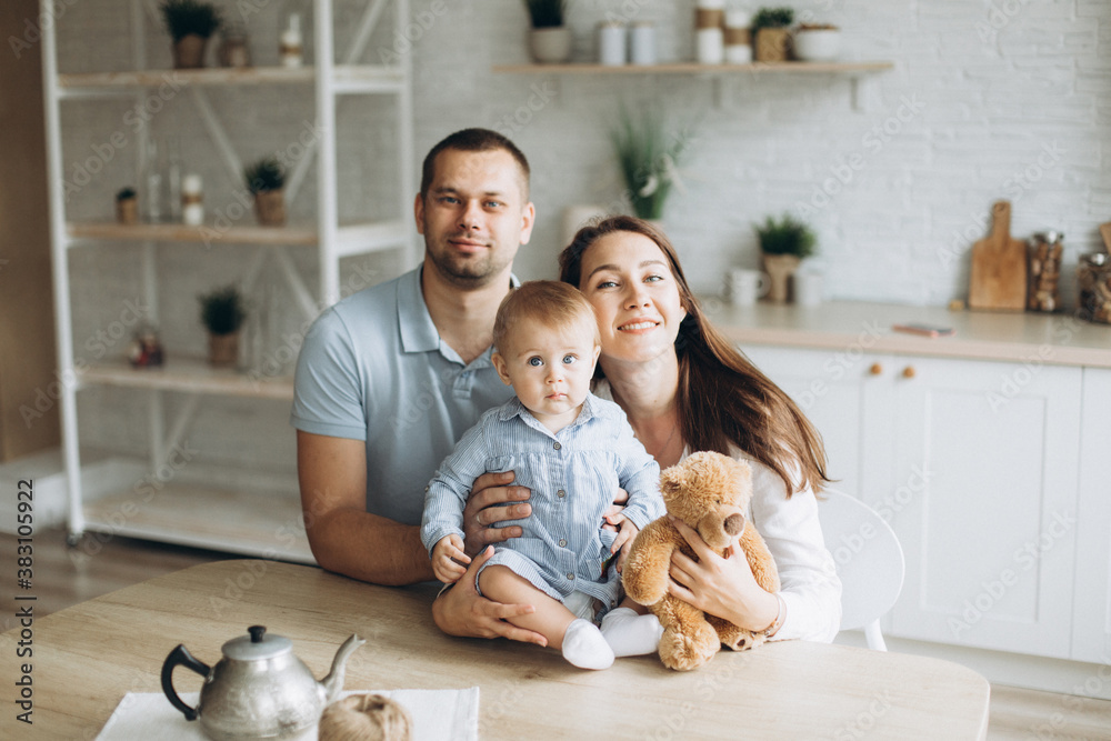Happy cheerful young family together with infant baby girl in kitchen at home