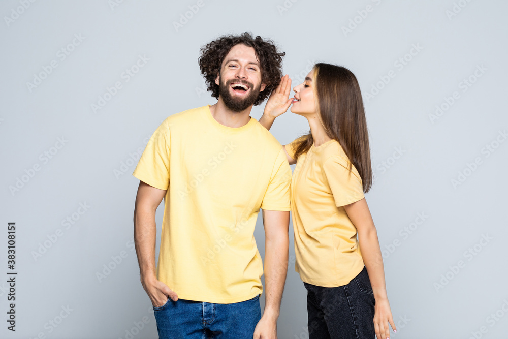 Excited couple telling secrets to each other standing isolated over gray background, Excited couple telling secrets to each other standing isolated over gray background,