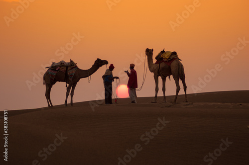 Man and a camel walking across sand dunes in Jaisalmer, Rajasthan, India. © Chetan Soni