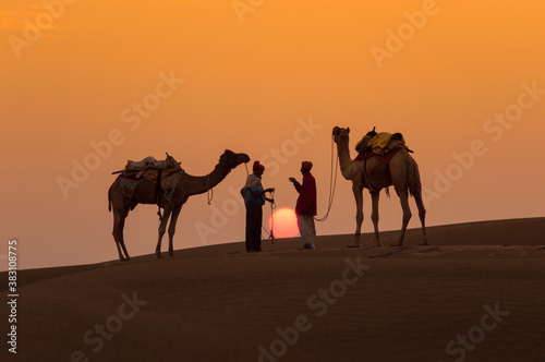 Man and a camel walking across sand dunes in Jaisalmer, Rajasthan, India. © Chetan Soni