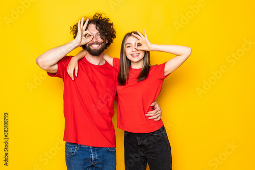 Excited beautiful couple wearing white t-shirts standing isolated over yellow background,