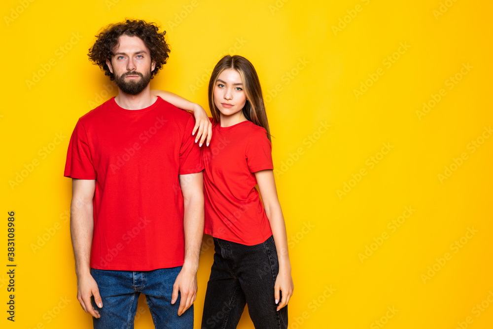 Fototapeta premium Portrait of content couple in basic clothing smiling at camera while woman putting her head on male shoulder over yellow background