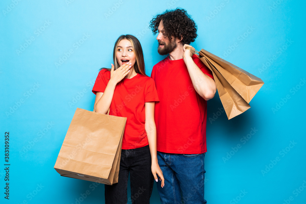 Happy young couple with shopping bags, standing close to each other with smile isolated on blue background. Happy young couple with shopping bags, standing close to each other with smile isolated on blue background.