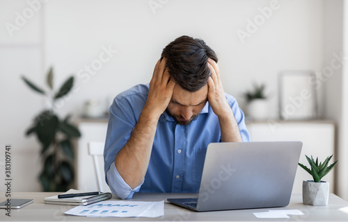 Business Problems. Desperate Millennial Businessman Sitting At Workplace In Office, Touching Head photo