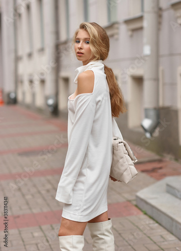 Elegant young female model with makeup and hairstyle standing and posing at city street. Autumn fashion