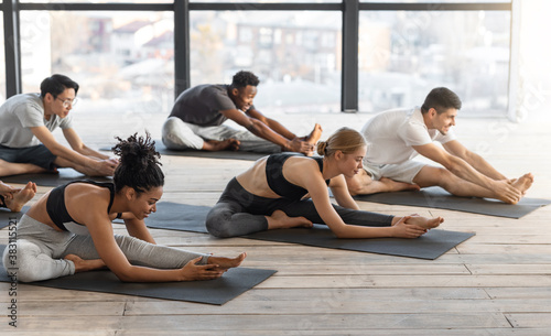 Canvas Print Diverse sporty men and women doing stretching exercises during group yoga lesson